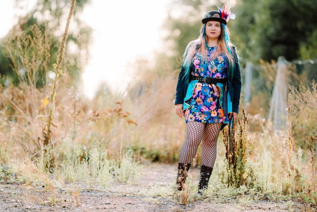 A girl in a steampunk outfit and bowler hat, standing in an overgrown outdoors area